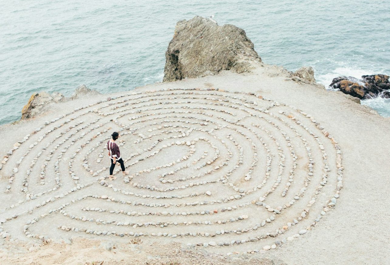 Gehe neue Wege für dich Eine Person geht durch ein Steinkreislabyrinth an einer Küste.